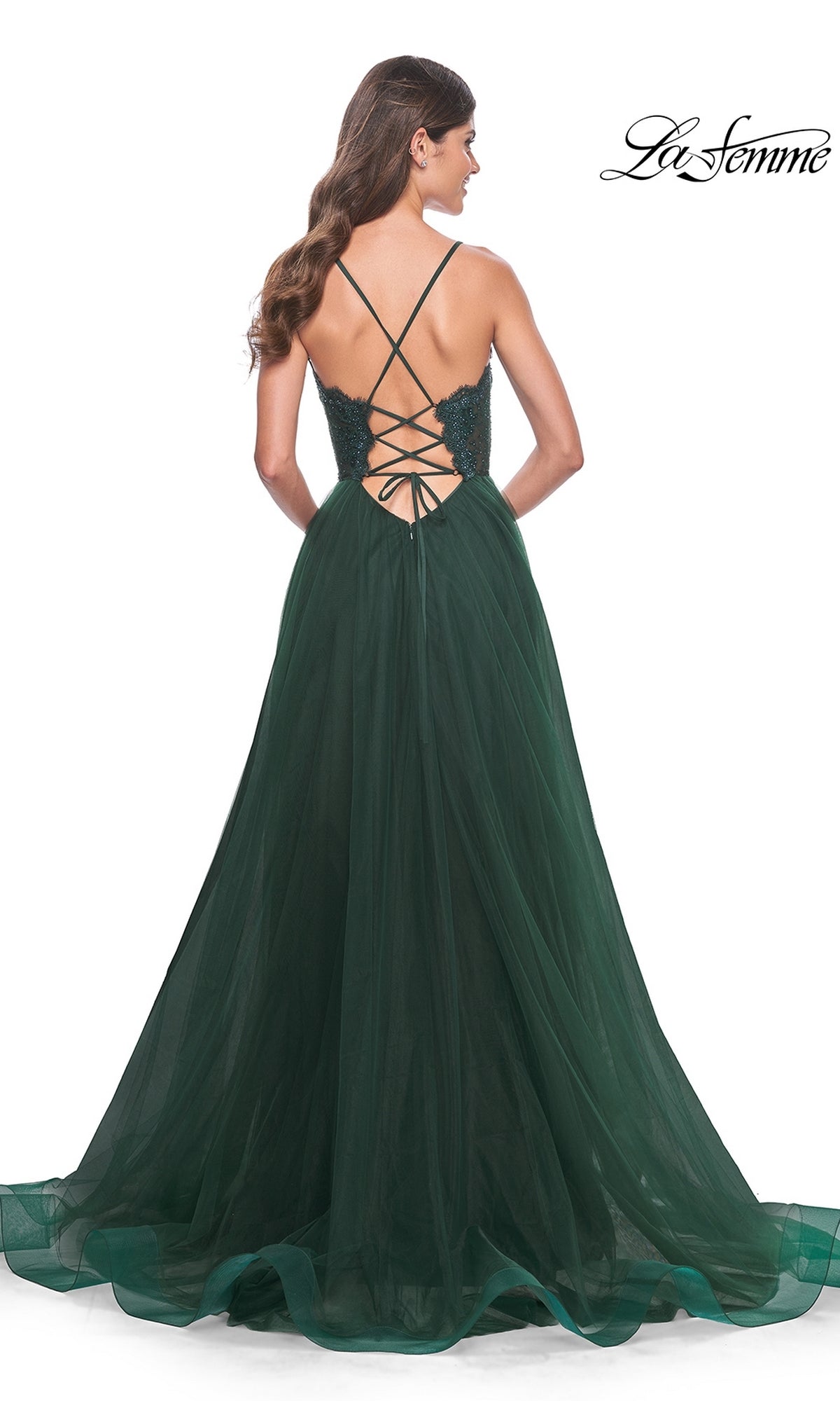 Woman in the La Femme Lace-Bodice Long A-Line Prom Dress 32306—an elegant dark green gown with a lace-up open back, crisscross straps, and a flowing tulle skirt—stands facing away, showcasing its sophisticated design.
